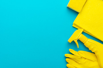 yellow cleanser in plastic container with spray, rubber protective gloves, sponge and cloths for cleaning on the turquoise blue background. flat lay image of yellow cleaning products with copy space
