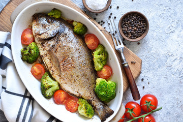 Baked dorado with spices, with broccoli and tomatoes on a concrete background.