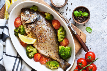 Baked dorado with spices, with broccoli and tomatoes on a concrete background.