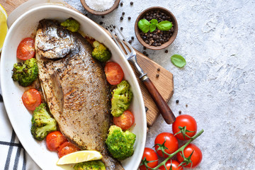 Baked dorado with spices, with broccoli and tomatoes on a concrete background.
