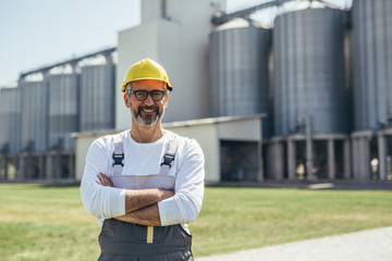 worker standing crossed arms in front of grain silo