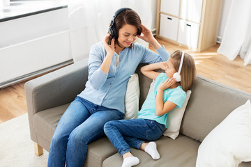 Obraz premium people, family and technology concept - happy mother and daughter in headphones listening to music at home