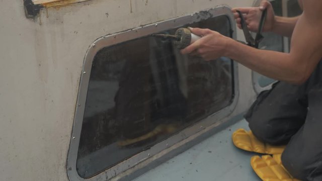 Carpenter re-sealing windows of wooden boat with sika flex mastic waterproof sealant.