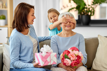 family, generation and birthday - mother and daughter greeting happy grandmother at home