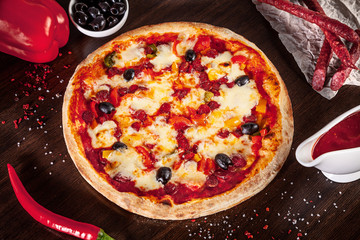 Top view on pizza with sausage and hot pepper, parmesan and white sauce with ingridients on brown wooden table. Picture for recipe or menu. Copy space for design. Served and cooked pizza.