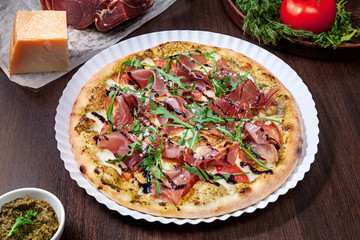 Top view on pizza with tomato, parmesan and prosciutto with white sauce with ingridients on brown wooden table. Picture for recipe or menu. Copy space for design. Served and cooked pizza.