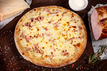Top view on pizza with ham, onion and parmesan and white sauce with ingridients on brown wooden table. Picture for recipe or menu. Copy space for design. Served and cooked pizza. Italian cuisine