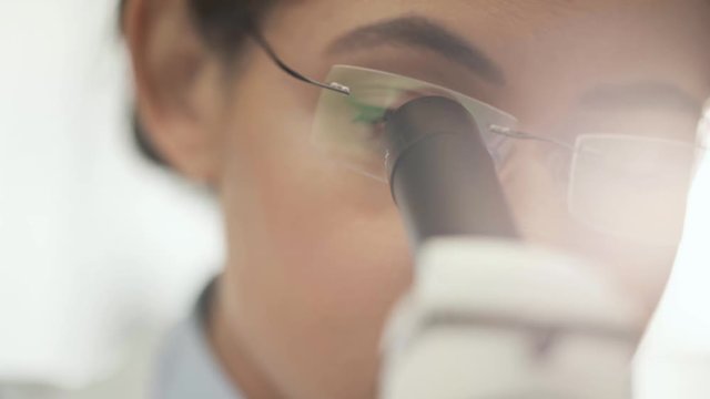 selective focus of african american scientist in glasses using microscope with sunlight on background