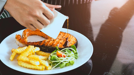 Chef is cooking salmon and Pour the delicious sauce and remove on the cooked salmon. By makeup with vegetables and french fries