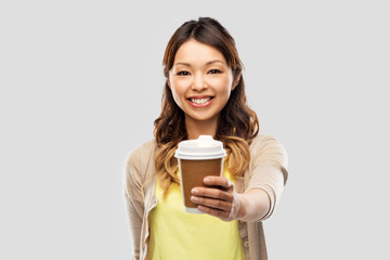 people and drinks concept - happy young asian woman drinking takeaway coffee from paper cup over grey background