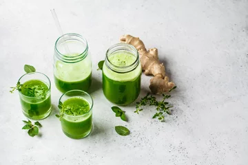 Tuinposter Green detox juice with ginger and mint in glasses and jars. © vaaseenaa