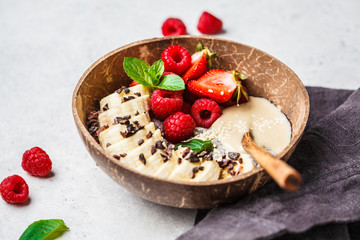 Chia pudding with berries, banana, peanut butter and cocoa nibs in coconut shell bowl.
