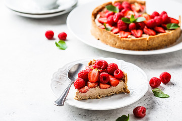 Piece of berry tart with raspberries, strawberries and cream on white plate.