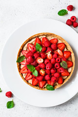 Whole berry tart with raspberries, strawberries and cream on white dish, top view.