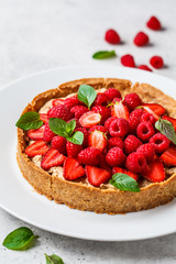 Whole berry tart with raspberries, strawberries and cream on white dish.