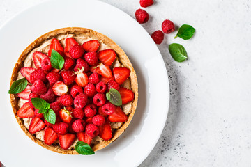 Whole berry tart with raspberries, strawberries and cream on white dish, top view. - obrazy, fototapety, plakaty