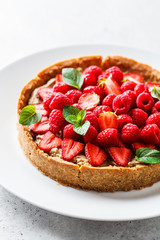 Whole berry tart with raspberries, strawberries and cream on white dish.