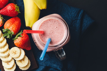 Smoothie with strawberry and banana in the jar at dark background, top view