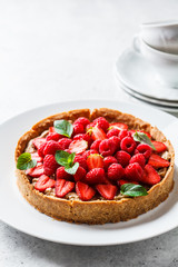 Whole berry tart with raspberries, strawberries and cream on white dish.