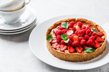 Whole berry tart with raspberries, strawberries and cream on white dish.