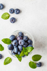 Chia pudding with blueberries and mint in glass on a white background, top view.