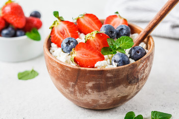 Cottage cheese with strawberries and blueberries in wooden bowl, light gray background.