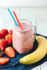 Smoothie with strawberry and banana in the jar at the white, wooden background with blue napkin