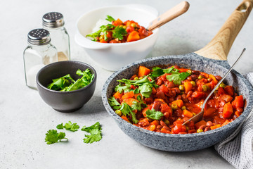 Vegan bean stew with tomatoes and rice in a pan over white background.