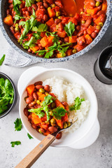 Vegan bean stew with tomatoes and rice in a pan over white background.