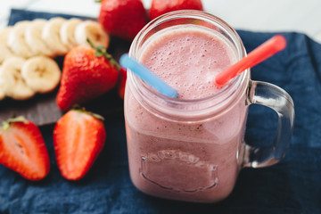 Smoothie with strawberry and banana in the jar at the white, wooden background with blue napkin