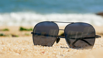 Dark sunglasses on the sandy beach in summer, close up