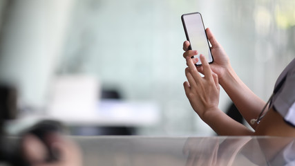 Cropped image of doctor using mobile phone in hands in office