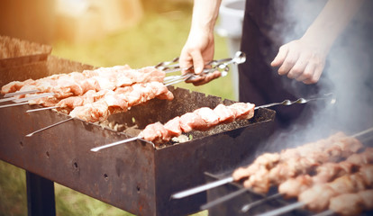 The chef prepares kebabs on metal skewers on the grill in the summer outdoors on a Sunny day.