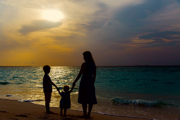 mother and two kids walking on beach at sunset