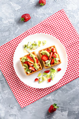 Belgian waffles with fruits strawberries and kiwi on white plate closeup. Tasty breakfast
