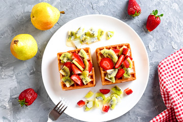 Belgian waffles with fruits strawberries and kiwi on white plate closeup. Tasty breakfast