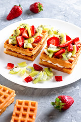 Belgian waffles with fruits strawberries and kiwi on white plate closeup. Tasty breakfast
