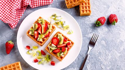 Belgian waffles with fruits strawberries and kiwi on white plate closeup. Tasty breakfast