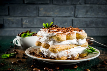 Homemade italian dessert tiramisu on plate, with cocoa and coffee beans, decorated with mint, dark...