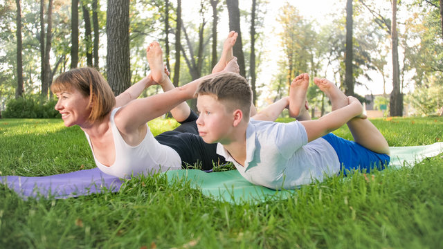 Photo of middle aged woman with 12 years old teenage boy practising yoga and meditating at park. family relaxing and doing fitness at nature