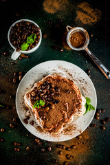 Homemade italian dessert tiramisu on plate, with cocoa and coffee beans, decorated with mint, dark green background copy space