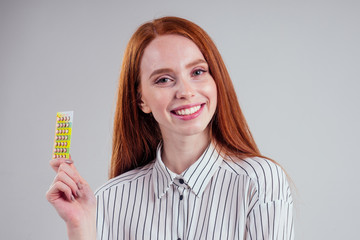 picture of young redhead businesswoman in striped shirt with one pack of pills white background studio