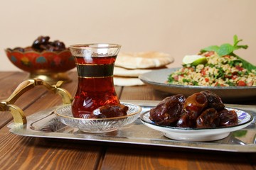 Traditional arabic Ramadan breakfast. Dates, tea in oriental glass on platter, tabbouleh, flat bread pita aish.