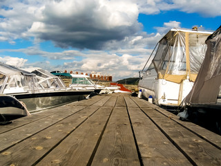 a pier of boards with boats, boats and yachts along it from two sides on a sunny day with clouds. close-up, bottom view, plank texture, summer vacation concept, water transport and fishing,