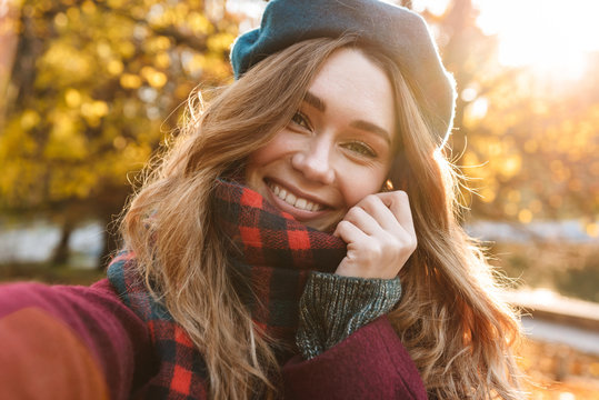 Beautiful happy young pretty woman walking outdoors in autumn spring park take a selfie by camera.