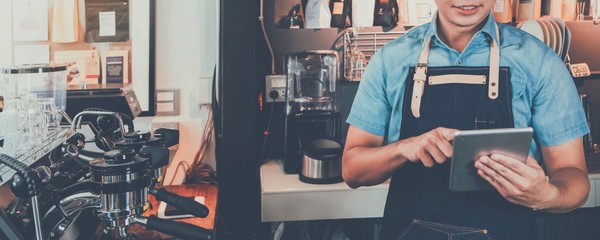 Young Asian man barista wear apron using tablet and receive order from customer at coffee shop banner background.Concept of cafe and coffee shop small business.