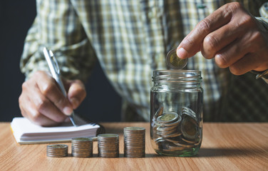 Men are Saint documents about save money and put coin in glass jar on desk.