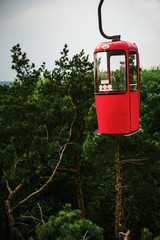 Red cabin of cableway on the green tree background in summer. Copy space.