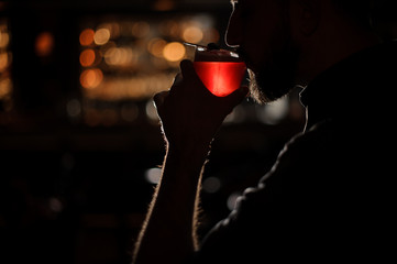 Bartender tasting a red transparent cocktail in the dark