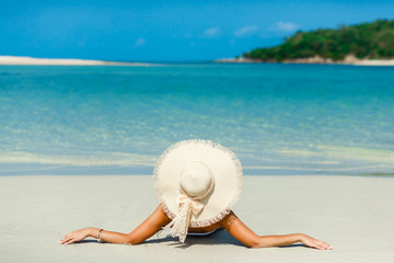 Fototapeta na wymiar Journey. Young beautiful lady in a straw hat, lying on the sand of the seashore with her back to the camera, rest, traveling, concept of perfect state of relaxation and freedom